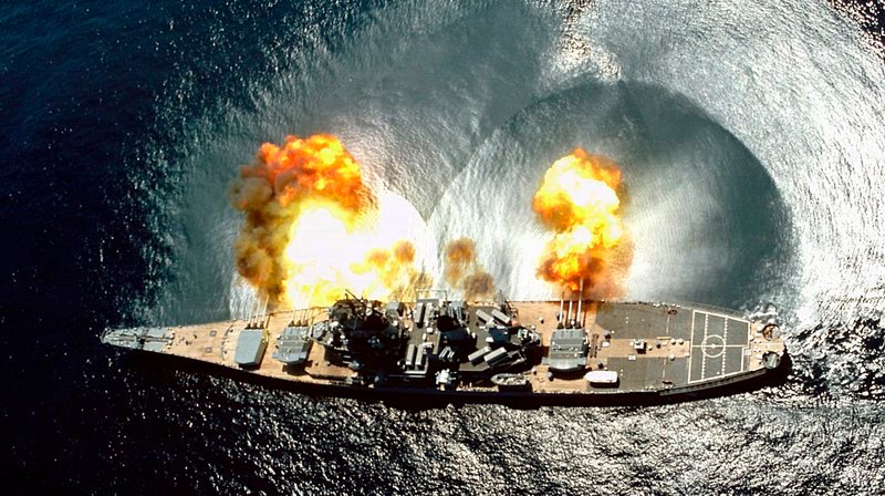 Vogelperspektive auf das Kriegsschiff USS IOWA, das während einer Übung in den Gewässern vor Vieques alle seine 15 Kanonen abfeuert. – Bild: HR/​BR/​NARA gemeinfrei