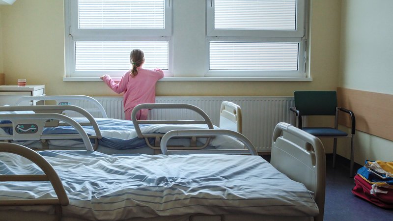 Viola (7 Jahre) steht im Krankenhauszimmer am Fenster und schaut hinaus, Landeskrankenhaus Steyr. – Bild: ORF