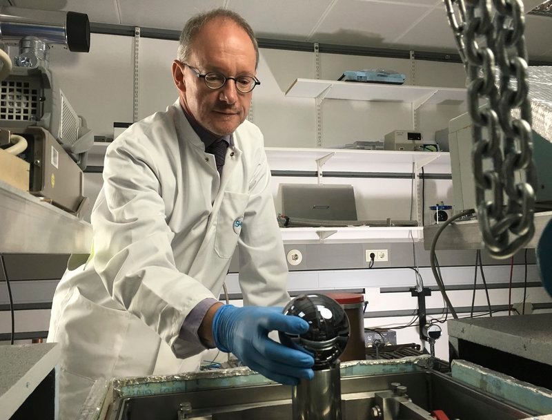 Dr. Arnold Nicolaus (PTB) setzt eine Siliziumkugel in das so genannte Kugel-Interferometer – Bild: MDR/​Längengrad Filmproduktion/​Dirk Gilson