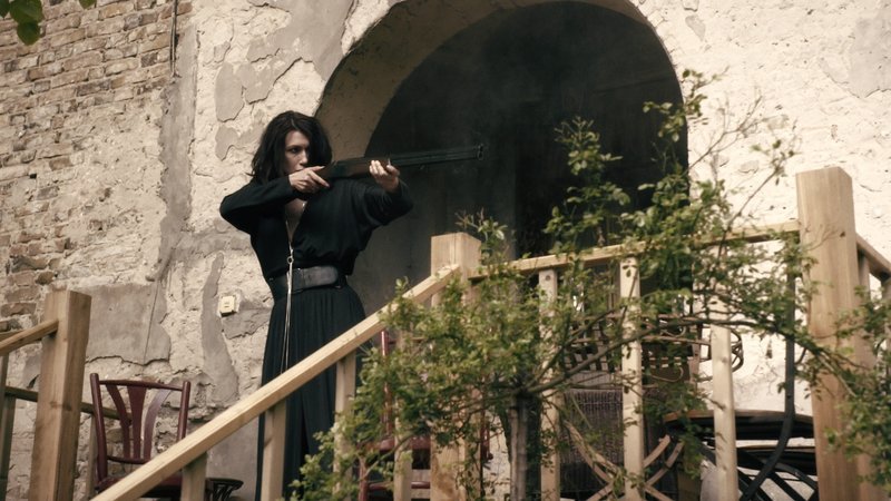 Anna (Claudia Mehnert) steht mit einem Gewehr auf der Veranda des Landhauses und zielt. – Bild: ZDF und Felix Cramer