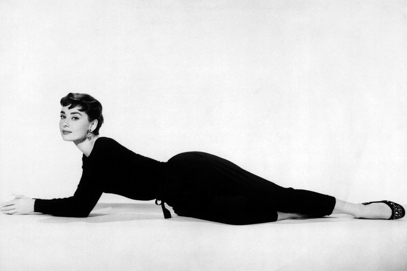 Audrey hat Spaß daran, begehrenswert zu sein, und Männer können sich in sie verlieben, ohne ihre Frauen zu verärgern: Hier räkelt sie sich in einem schwarzen Hosenanzug aus Billy Wilders Film „Sabrina“ aus dem Jahr 1954. – Bild: 2002 Getty Images/​Paramount Pictures
