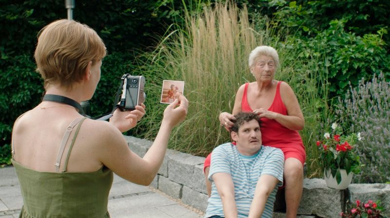 Frank (Felix Lukas Mühlen) und Gretel (Brigitte Janner) stellen mit Christines (Caroline Junghanns, li.) Hilfe ein Familienfoto nach. – Bild: SWR/​Filmakademie BW