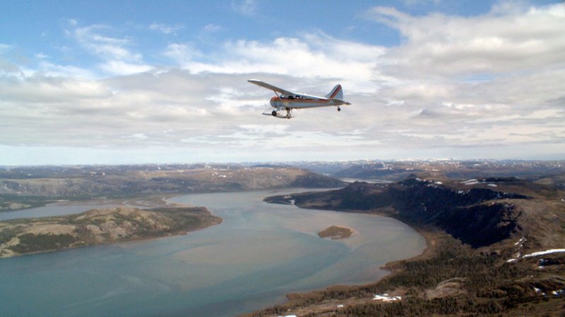 Der erste Inuit-Pilot Johnny May kreist in seinem Flugzeug über die karge Landschaft des nördlichsten Teils der kanadischen Arktis und lässt zur Freude der Kinder einen alten Brauch wieder aufleben. – Bild: ARTE France /​ © Office National du Film du Canada