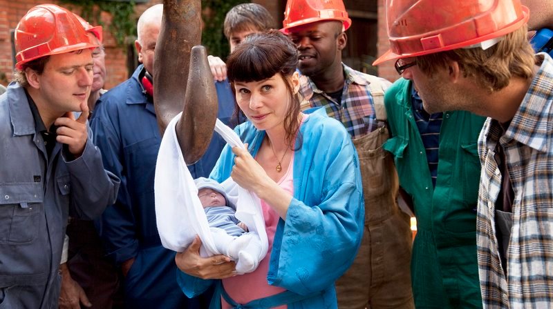 Baby Tony wird mit dem Kran in die Arme von und Mutter Sissy (Rifka Lodeizen) herunter gelassen. Die Bauarbeiter staunen. – Bild: MDR/​Victor Arnolds