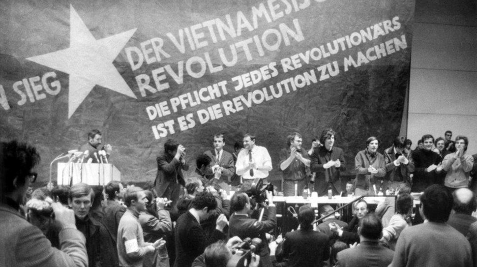 17.02.1968, Berlin: Etwa 3000 Personen, meist Studenten, nehmen an der vom Sozialistischen Deutschen Studentenbund (SDS) durchgeführten «Internationalen Vietnam-Konferenz» in der TU teil. Auf dem Bild vor einer übergroßen Vietkong-Fahne am Tisch stehend sind zu sehen:v.l.n.r. K.D. Wolff (am Rednerpult), Dr. Klaus Meschkat, Dr. Johannes Agnoli, Christian Semmler, Gaston Salvatore, Rudi Dutschke, Günther Ament, Kurt Steinhaus und Tariq Ali. Mit dem Vietnam-Kongress vor 50 Jahren erreichte der Studentenprotest in Deutschland seinen politischen Höhepunkt. – Bild: WDR / dpa / Volkmar Hoffmann