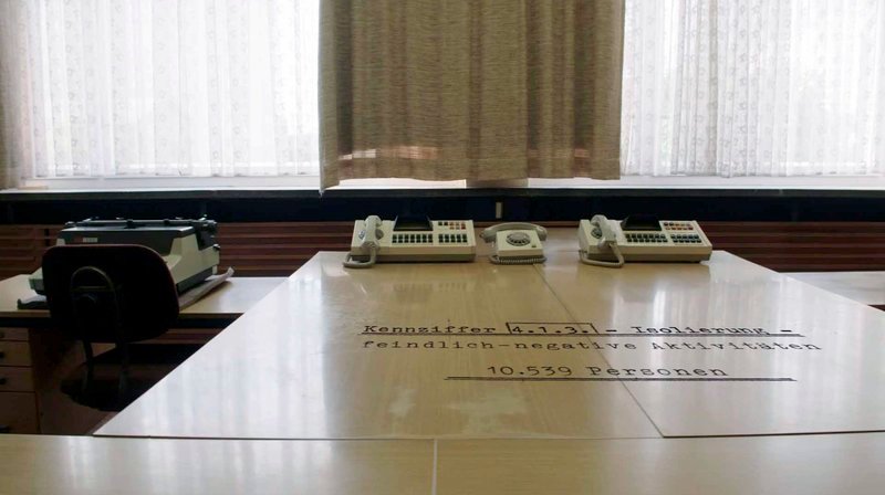 Es ist ein unheimlicher Plan für den „Tag  X“: Mit einem speziellen Codewort an alle 211 MfS-Kreisdienststellen wird eine ungeheurere Maschinerie in Gang gesetzt. DDR-weit werden innerhalb von 24 Stunden über 2.900 Personen festgenommen und über 10.000 in vorbereitete Isolierungslager verschleppt. Weitere 72.000 Bürger werden verstärkt überwacht. So sieht es die streng geheime „Direktive 1/​67“ vor. – Im Büro der Staatssicherheit in Berlin – Bild: rbb/​Scoopfilms