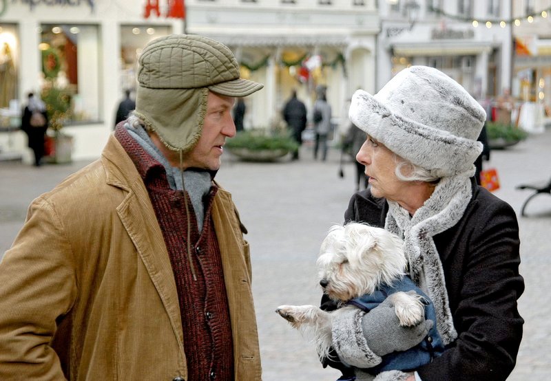 Elvira Hertzfeld (Rosemarie Fendel) will nicht, dass Straßenmusikant Paul (Miroslav Nemec) seinem Hund erlaubt, mit ihrer Hündin Minou anzubändeln. Auf viel Verständnis bei Paul stößt sie dabei nicht. Aber im übrigen ist der Mann überaschend höflich! – Bild: SWR/​Schweigert