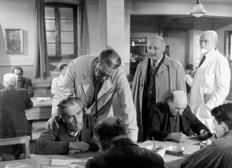 Patientenbesuch: Max Werner Lenz als Patient (sitzend), Heinz Woester als Dr. Laduner (darüber gebeugt), Heinrich Gretler als Wachtmeister Studer (2.v.r.) – Bild: SF