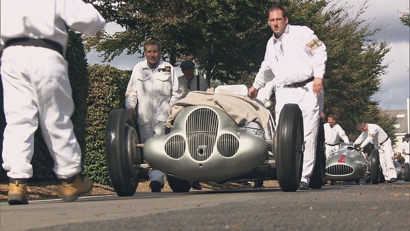 Das PS-Festival in Goodwood bietet einen einmaligen Rahmen für die Wiederauferstehung der Silberpfeile: Es ist wie eine Zeitreise in die Mitte des vorigen Jahrhunderts; dazu gehört auch, dass Fahrer, Monteure und Zuschauer dazu angehalten sind, sich zu kleiden wie in den Vierziger- oder Fünfzigerjahren. – Bild: N24 Doku Das PS-Festival in Goodwood bietet einen einmaligen Rahmen für die Wiederauferstehung der Silberpfeile: Es ist wie eine Zeitreise in die Mitte des vorigen Jahrhunderts; dazu gehört auch, dass Fahrer, Monteure und Zuschauer dazu angehalten sind, sich zu kleiden wie in den Vierziger- oder Fünfzigerjahren. – Bild: N24 Doku