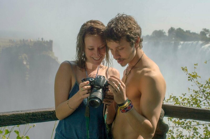 Gabriel (João Pedro Zappa) und Cristina (Caroline Abras) machen Fotos vor den Victoriafällen. – Bild: Damned Films /​ © Damned Films