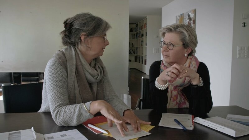 Die Autorin Luzia Schmid (links) lässt sich von ihrer Schwester Andrea Hodel-Schmid erklären, wieso sie in Zug sehr viel weniger Steuern zahlen würde als in ihrer Wahlheimat Köln. – Bild: ZDF und Hajo Schomerus