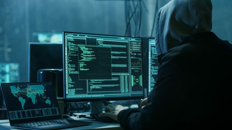 Gefährlicher vermummter Hacker bricht in die Datenserver der Regierung ein und infiziert ihr System mit einem Virus. Sein Versteck hat dunkle Atmosphäre, mehrere Bildschirme, Kabel überall. – Bild: Shutterstock