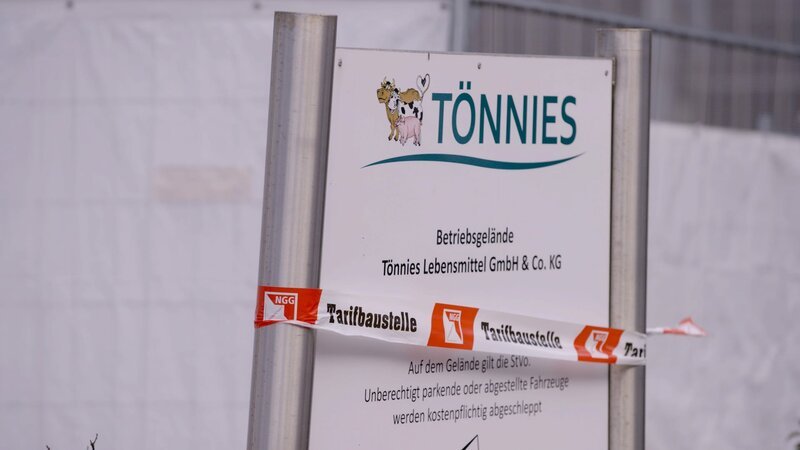 Unter dem Tönnies Firmenschild haben Demonstrierende ein Flatterband mit Aufschrift „Tarifbaustelle“ angebracht. – Bild: ZDF und Ralf Huppke./Ralf Huppke Unter dem Tönnies Firmenschild haben Demonstrierende ein Flatterband mit Aufschrift „Tarifbaustelle“ angebracht. – Bild: ZDF und Ralf Huppke./Ralf Huppke