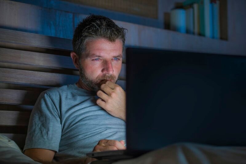 Stockfotografie junger attraktiver und entspannter internetsüchtiger Mann, der sich bis spät in die Nacht auf dem Bett mit Laptop in Social-Media-Sucht oder Workaholic-Geschäftsmann-Konzept konzentriert – Bild: Depositphotos