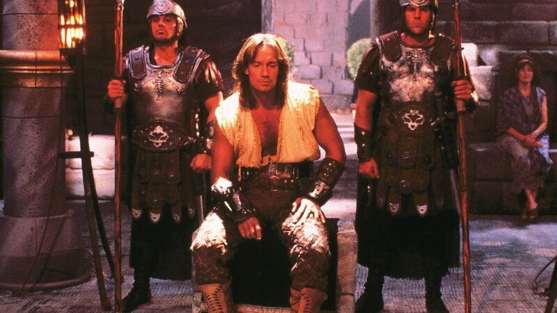 Hercules (Kevin Sorbo, Mi.) wird wegen Totschlages, Verächtlichmachung der Götter und Aufwiegelung angeklagt. Er erklärt sich in allen Anklagepunkten als unschuldig (li. und re. Komparsen). – Bild: TVNOW