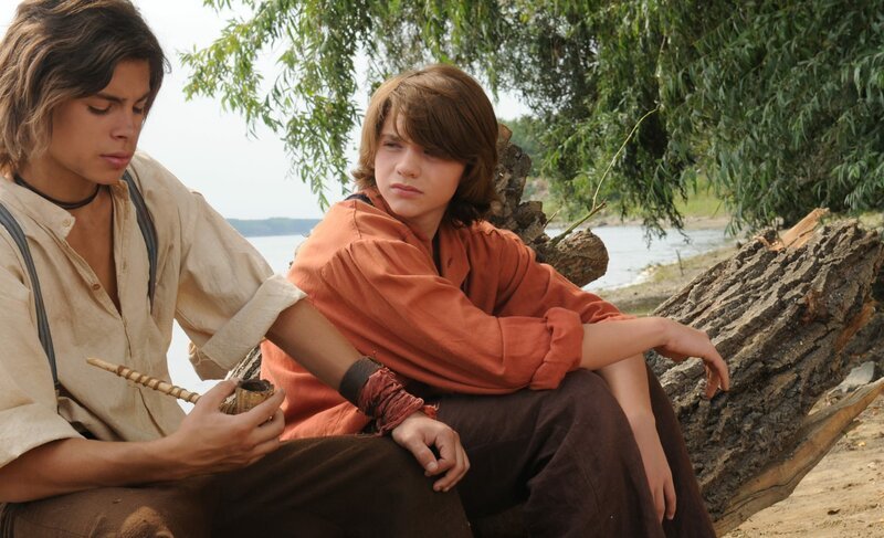 Tom Sawyer (Joel Courtney, r.) und Huckleberry Finn (Jake T. Austin, l.) sind unzertrennliche Freunde. Sie sitzen am Ufer des Mississippi und hecken neue Abenteuer aus. – Bild: ZDF und Simon Versano.