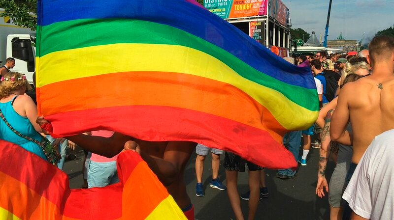 Mann schwingt Regenbogenflaggen auf gay pride Festival in Berlin. – Bild: WDR/​BlackBoxGuild
