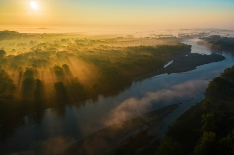 Der Sonnenuntergang spiegelt sich malerisch im Fluss wider und taucht das Ufer in einen goldenen Schleier. – Bild: Goran Safarek