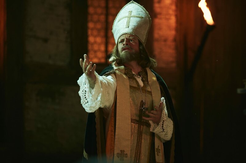 Der Bischof von Arl (Max Giermann) lässt (fast) nichts anbrennen und antwortet einer Hexe auf dem Scheiterhaufen im Rahmen eines Musicals. – Bild: ZDF und Kristof Galgoczi Nemeth