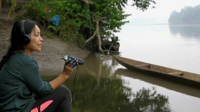 Radio-Frauen aus dem Regenwald Mit Mikro und Rekorder gegen Ausbeutung Am Flussufer berichtet die Radio-Frau über das Leben im Regenwald SRF/​ZDF – Bild: SRF2