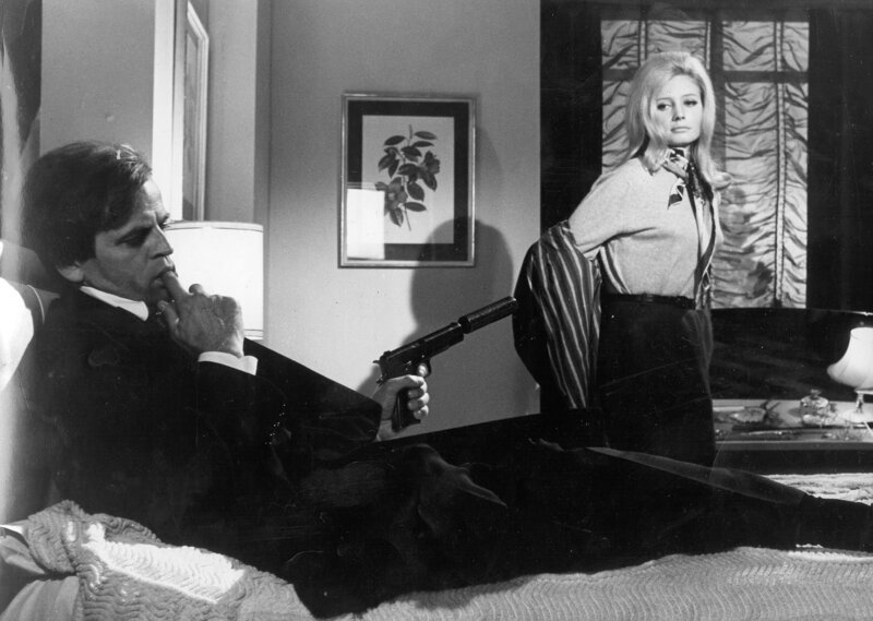 Der Ganove Kane (Klaus Kinski, li.) hält die Sekretärin Hope (Catherine von Schell, re.) mit einer Waffe in Schach … – Bild: Tobis Film Der Ganove Kane (Klaus Kinski, li.) hält die Sekretärin Hope (Catherine von Schell, re.) mit einer Waffe in Schach … – Bild: Tobis Film