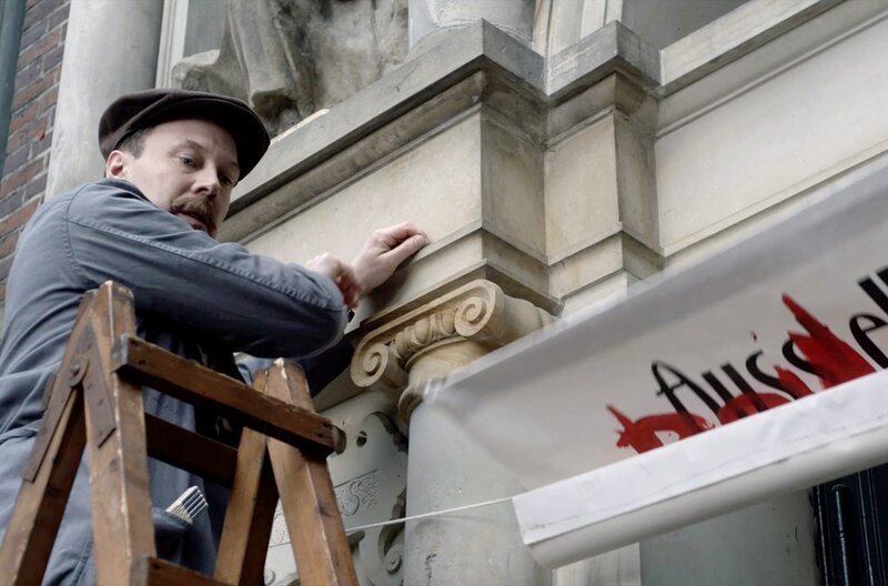 Hausmeister Wilhelm Werner (Tim Porath) entfernt ein antisemitisches Transparent vom Eingangstor der Hamburger Kunsthalle. – Bild: NDR /​ © Daniel Leibold/​Marlene Film /​ © Daniel Leibold/​Marlene Film