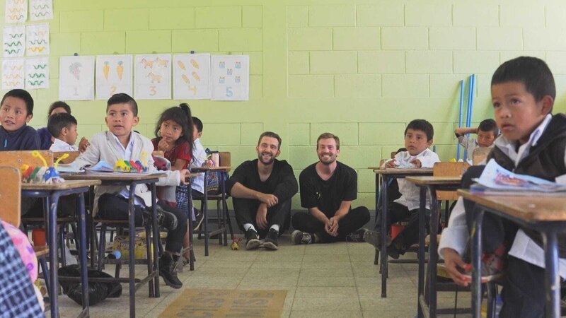 Nono Konopka (l.) und Maximilian Jabs sitzen mit vielen Kindern in einem Klassenzimmer   – Bild: RTL /​ © Maximilian Jabs & Nono Jannik Konopka GbR