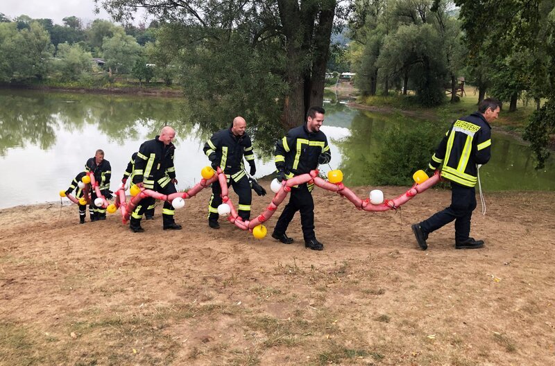 Mitglieder der Feuerwehr testen einen Haarschlauch an einem See. – Bild: SWR /​ Mitglieder der Feuerwehr testen einen Haarschlauch an einem See.
