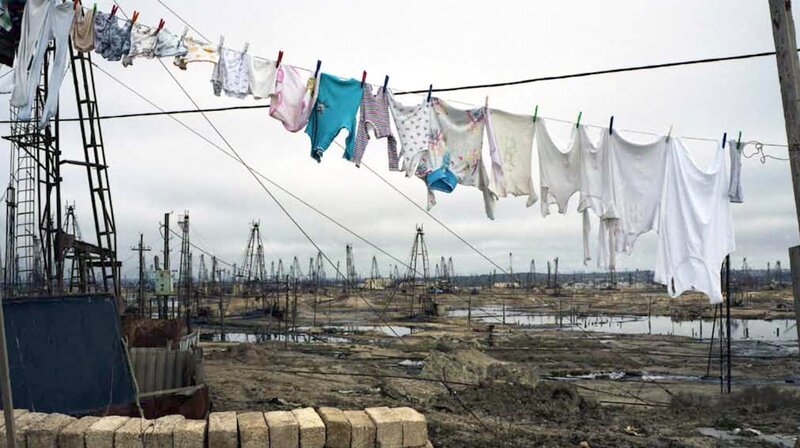Eine Wäscheleine voller Kinderkleidung, im Hintergrund Ölförderstellen und verwüstete Landschaft in Baku/​Aserbeidschan (Liquid Land, 2008; Künstlerin: Rena Effendi). – Bild: ORF/​2022 NAVIGATOR FILM & Vive LaDok