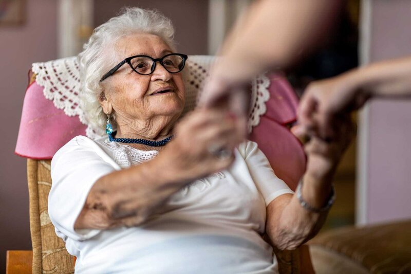 Female home carer supporting old woman to stand up from the armchair at care home – Bild: ntv