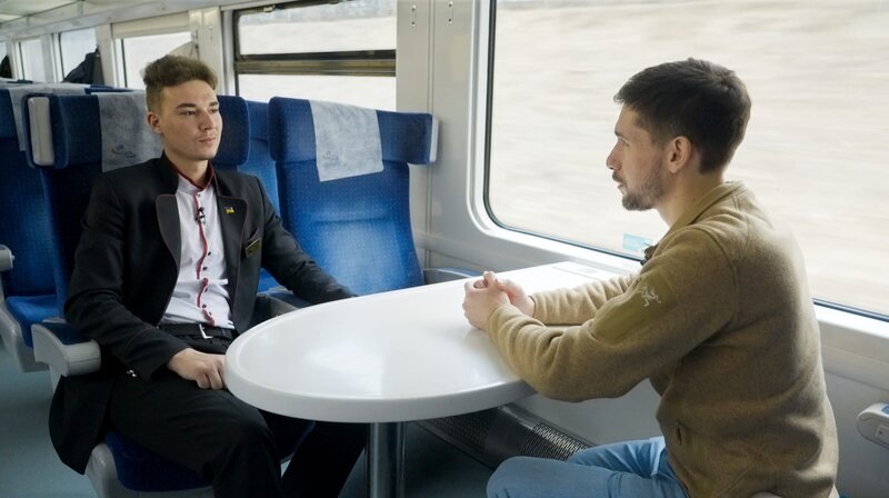 Ilja Prudnyk (l) arbeitet als Schaffner für die ukrainische Bahn. Die Züge fahren auch mitten im Krieg. Gegenüber ARD-Korrespondent Vassili Golod vergleicht er das Bahnnetz der Ukraine mit den Adern in einem Körper. – Bild: WDR/​Robin Drescher