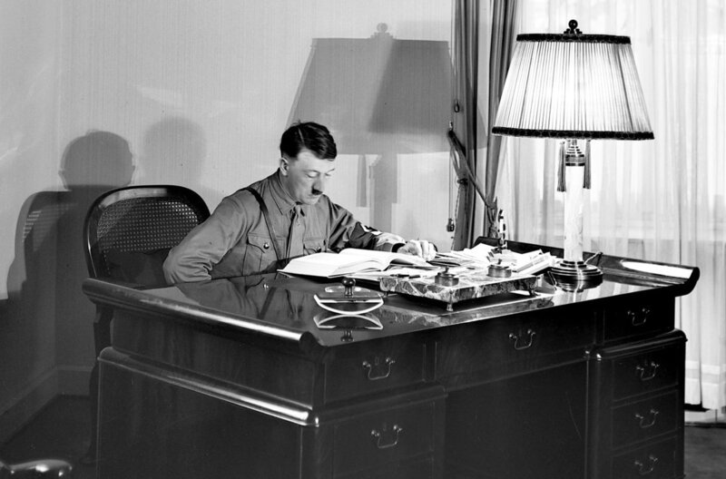 Hitler liest an seinem Schreibtisch in einem Buch. – Bild: National Archives, USA /​ © National Archives, USA