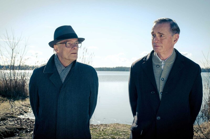 Honecker (Edgar Selge, li.) und Holmer (Hans Uwe Bauer, re.) spazieren am See entlang. – Bild: ZDF/​arte/​Conny Klein