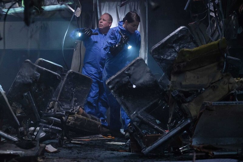 Der Ermittler Tony James (gespielt von Tim O’Halloran) wird von einem anderen FAA-Ermittler flankiert, während er in der verkohlten Flugzeugkabine des Uni Air Fluges 873 nach Hinweisen sucht.(Cineflix 2018/​Darren Goldstein) – Bild: National Geographic