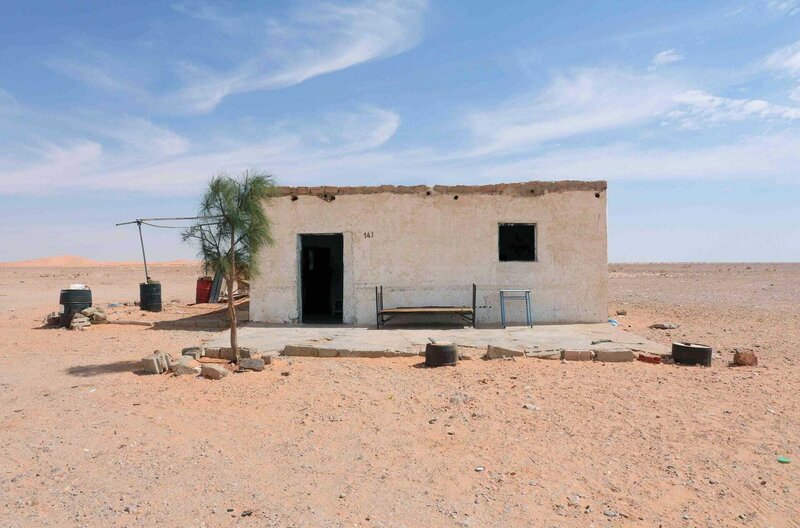 Malika besitzt einen Imbiss an einem Highway, der seit drei Jahrzehnten durch Algerien führt. Er ist umgeben von Sand, Dünen und Geröll. Im Umkreis von mehreren Kilometern lebt keine Menschenseele. – Bild: Hassen Ferhani /​ Malika besitzt einen Imbiss an einem Highway, der seit drei Jahrzehnten durch Algerien führt. Er ist umgeben von Sand, Dünen und Geröll. Im Umkreis von mehreren Kilometern lebt keine Menschenseele.