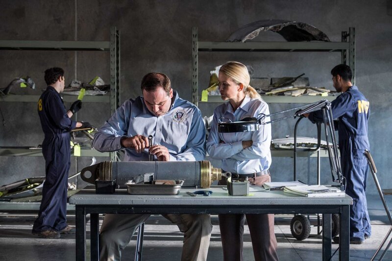 Ayr, ON – REENACTMENT – Lorenda Ward, played by Marnie Robinson and an NTSB crash investigator, played by Dimitri Vantis, inspect a cracked actuator as other NSTB crash investigators, played by background performers, assess evidence. (Cineflix 2017/​Darren Goldstein) – Bild: Darren Goldstein /​ Cineflix 2017 /​ Cineflix 2017/​Darren Goldstein