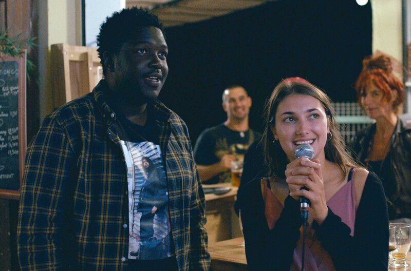 Chérif (Salif Cissé) und Héléna (Ana Blagojevic) singen an ihrem letzten gemeinsamen Abend unbeschwert Karaoke in der kleinen Bar am Campingplatz. – Bild: Geko Films/ARTE France / © Geko Films/ARTE France Chérif (Salif Cissé) und Héléna (Ana Blagojevic) singen an ihrem letzten gemeinsamen Abend unbeschwert Karaoke in der kleinen Bar am Campingplatz. – Bild: Geko Films/ARTE France / © Geko Films/ARTE France