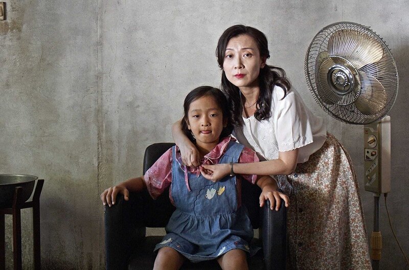 Die Mutter (Jiali Wang) hat den siebenjährigen Yan (Bowen Hu) als Mädchen verkleidet, bevor der Beamte für Bevölkerungsplanung eintrifft. – Bild: Hanxiong Bo /​ Die Mutter (Jiali Wang) hat den siebenjährigen Yan (Bowen Hu) als Mädchen verkleidet, bevor der Beamte für Bevölkerungsplanung eintrifft.