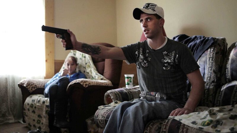 Sergeant Nathan Harris zuhause mit seiner Waffe. Im Hintergrund seine Frau Ashley – Bild: GEO TELEVISION