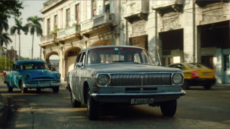 Der Ostberliner Matthias arbeitet routiniert in einer Werbeagentur vor sich hin. Eines Tages jedoch soll er die Asche seiner Mutter, einer überzeugten Sozialistin, an einem besonderen Ort verstreuen. Dafür muss er sich auf eine unbewohnte Insel vor Kuba begeben, die Fidel Castro einst der DDR schenkte: Cayo Ernesto Thälmann – Ernesto’s Island. – Matthias (Max Riemelt) und Sofia (Marion Duranona) fahren mit dem Auto durch Havanna. – Bild: rbb/​NEUE HEIMATFILMPRODUKTION GmbH