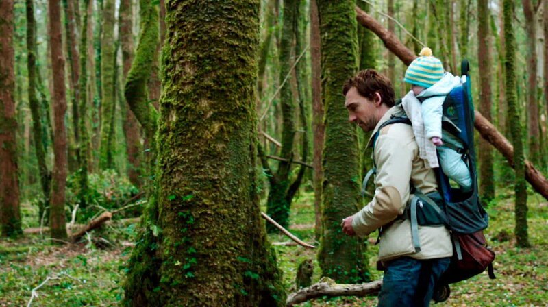 Adam (Joseph Mawle) soll im Auftrag eines Holzkonzerns den Zustand des Urwalds untersuchen. Mit Baby Finn auf dem Rücken macht er sich auf zu ersten Erkundungsgängen unter die düsteren alten Bäume. – Bild: MDR/​MFA+ FilmDistribution e.K.