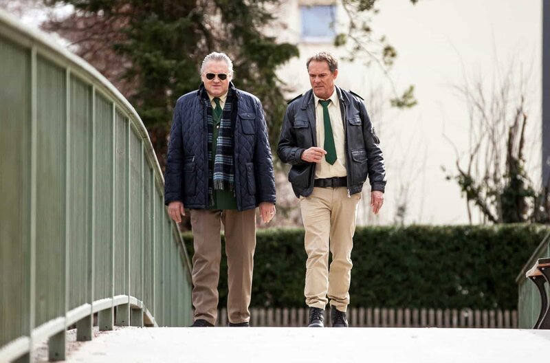 Hubert (Christian Tramitz, rechts) und Girwidz (Michael Brandner) haben ein vertrauliches Gespräch bei einem Spaziergang durch den Park. – Bild: ARD/​BR/​TMG/​Chris Hirschhäuser