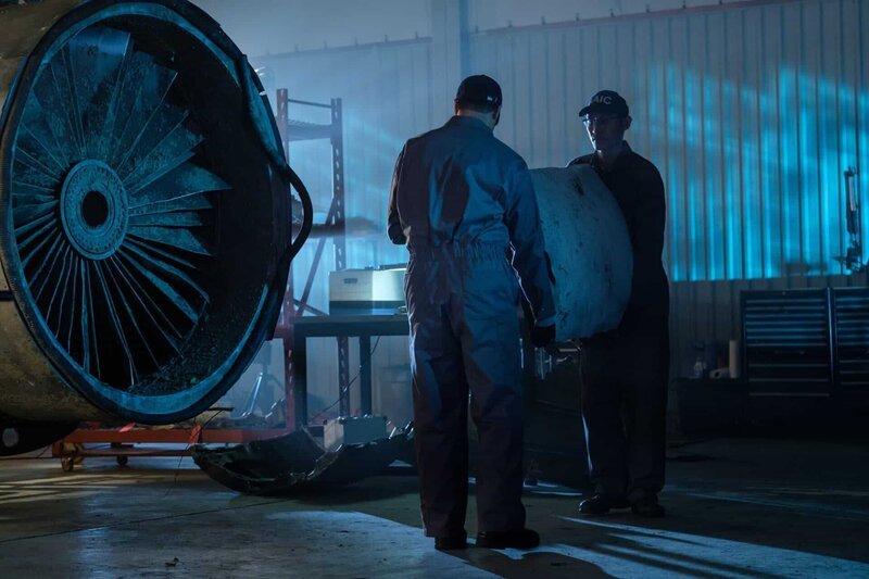 Arbeiter (gespielt von Schauspielern im Hintergrund) tragen Wrackteile von Flug 140 der China Airlines. – Bild: Cineflix /​ Darren Goldstein