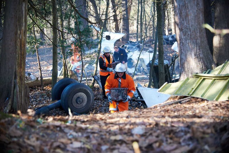 Investigator Bob Benzon (played by Kevin Carter) and recovery workers (played by background actors) sort through the debris of Alitalia flight 404. – Bild: Cineflix /​ Darren Goldstein