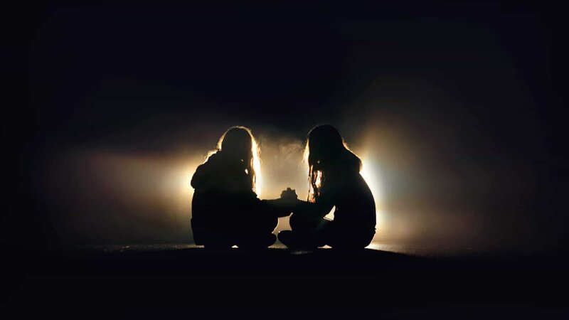 Silhouette of two girls sitting on the pavement of a road, facing, holding hands in the dark – Bild: Sol de Zuasnabar Brebbia /​ Getty Images /​ GettyImages-503974420 /​ © 2016 Sol de Zuasnabar Brebbia