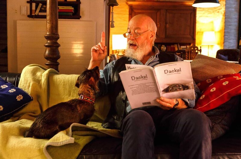 Hundeschule einmal anders: Reinhard Bielefelder (Bill Mockridge, r.) liest Dackel Yoda aus dem „Dackelbuch“ vor. – Bild: ARD/​Kai Schulz