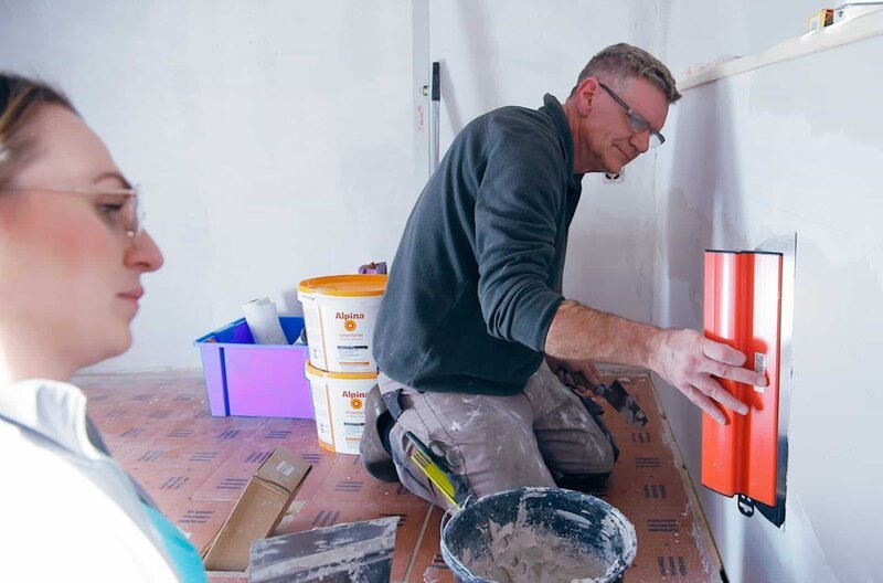 „Schön flach ansetzen!“ Malermeisterin Nina gibt Christoph Spachteltipps für schön glatte Wände. – Bild: NDR/​Florian Melzer/​nonfictionplanet