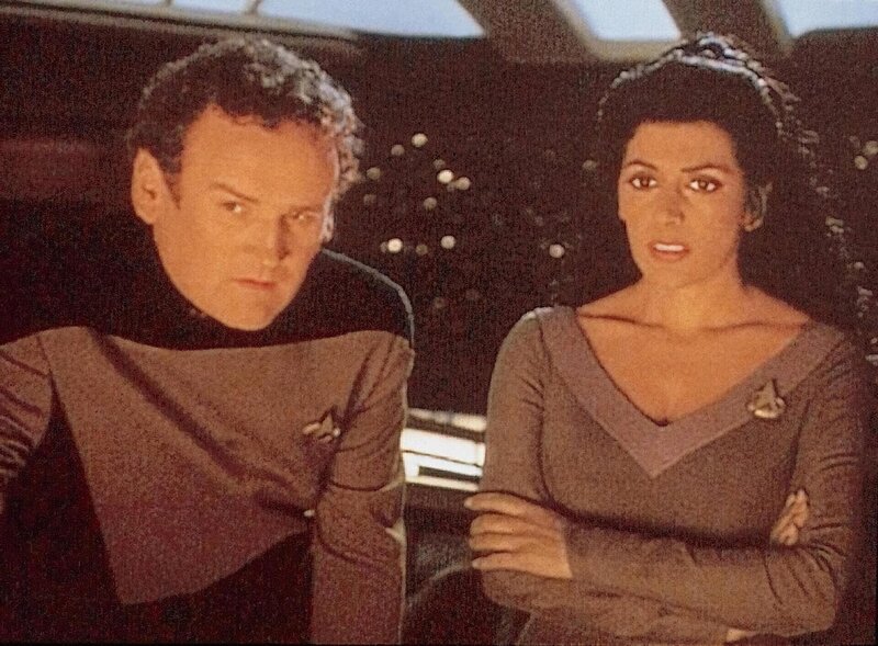 O’Brian (Com Meaney) und Troi (Marina Sirtis) stehen ratlos vor der Instrumententafel … – Bild: SYFY