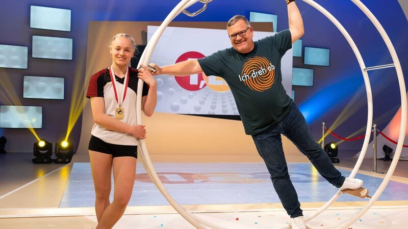 Von Junioren-Weltmeisterin Lea Gmeiner (l.) lässt sich Elton bei „1, 2 oder 3“ heute einige Tricks mit dem Rhönrad zeigen. – Bild: ZDF und Ralf Wilschewski./​Ralf Wilschewski
