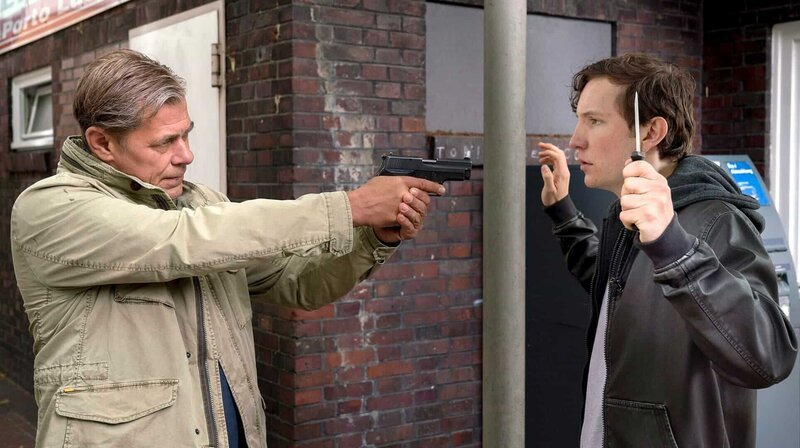 Finn (Sven Martinek, l.) befiehlt Niko Bruhn (Leonard Carow, r.), mit gezogener Waffe, das Messer fallen zu lassen. – Bild: ARD/​Georges Pauly